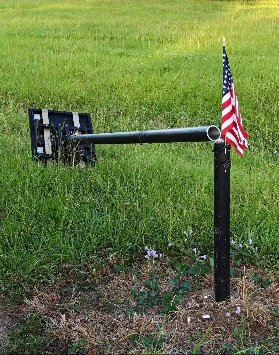 A small American flag fastened to a roadside surveillance camera pole, the camera turned away from the road